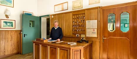 Un mostrador de recepción con detalles de madera, un perchero de llaves en la pared, diplomas enmarcados y una puerta con panel de vidrio.