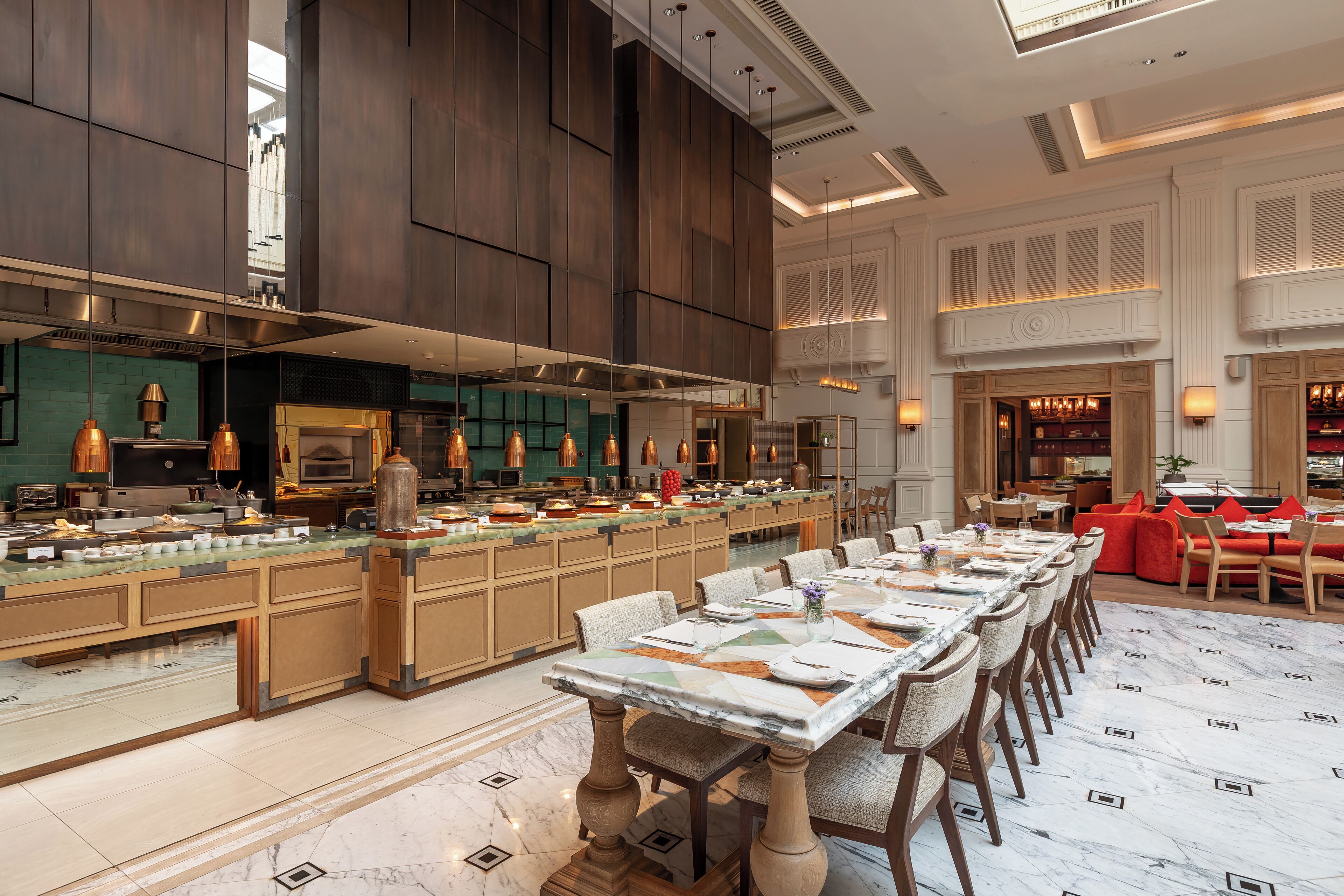 A spacious dining area with a long table set for a meal, a kitchen area with modern appliances, and a seating area with red sofas.