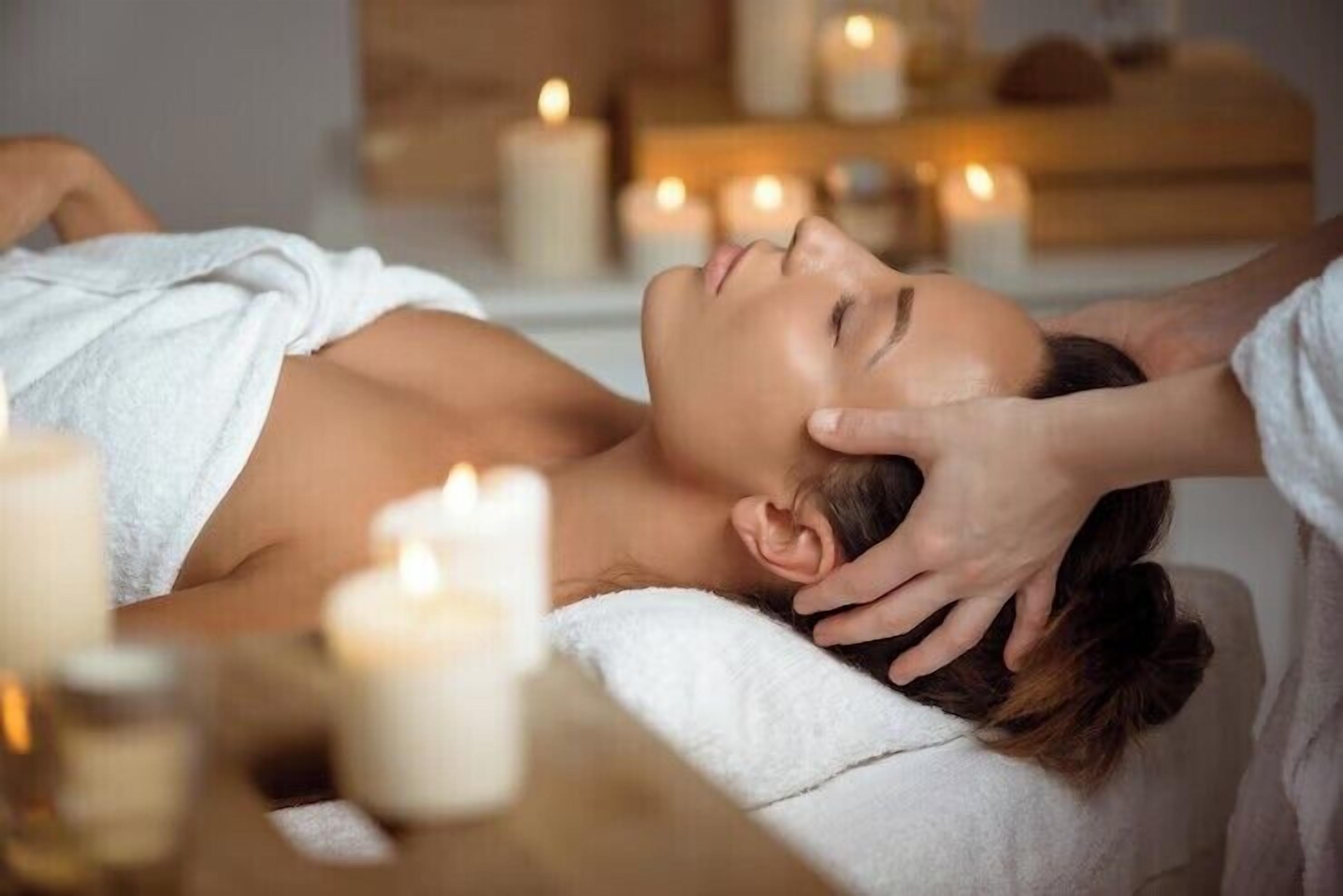 A person receiving a massage in a room with candles and a wooden side table.