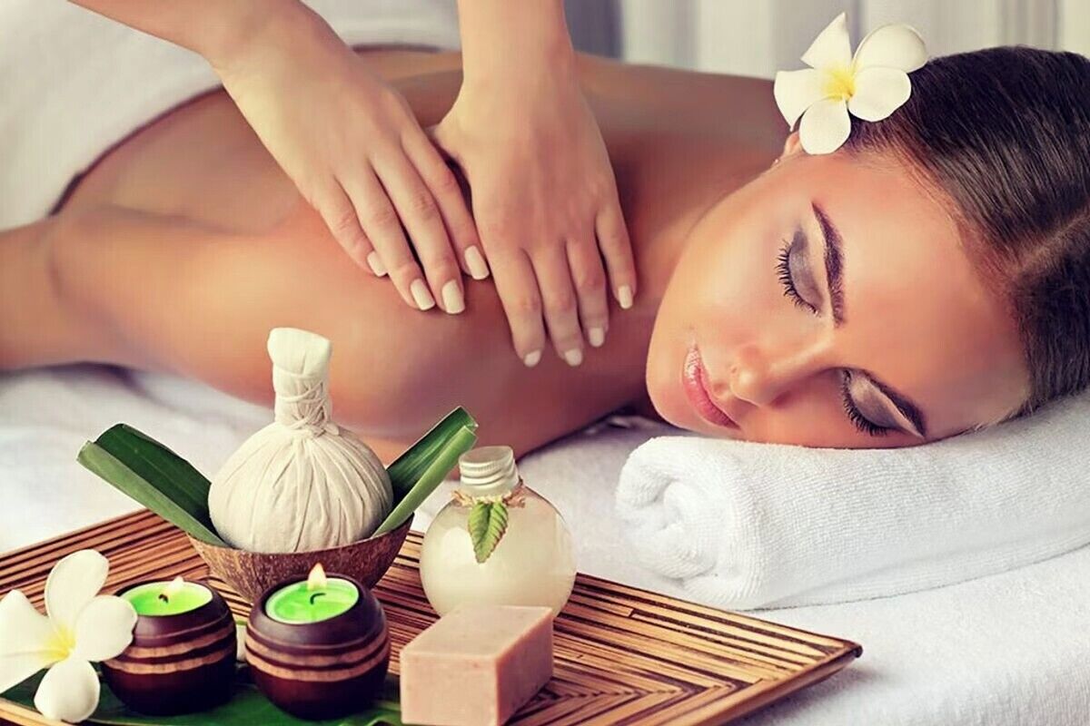Una persona recibiendo un masaje, con diversos productos de spa como velas, una botella y aceite de masaje sobre una bandeja.