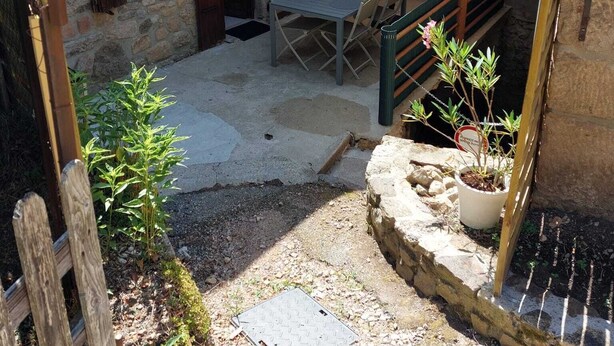 Un bâtiment en pierre doté d’un patio comprenant une table et des chaises, un petit escalier et un pot de fleurs.