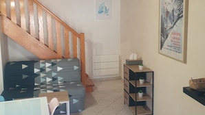 Un salon chaleureux avec un escalier en bois, un canapé à motifs, une petite table et une affiche accrochée au mur.