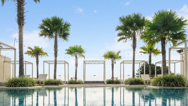 A pool area with palm trees, lounge chairs, and a clear sky. - Askara by Kozystay - Ciumbuleuit (Bandung)