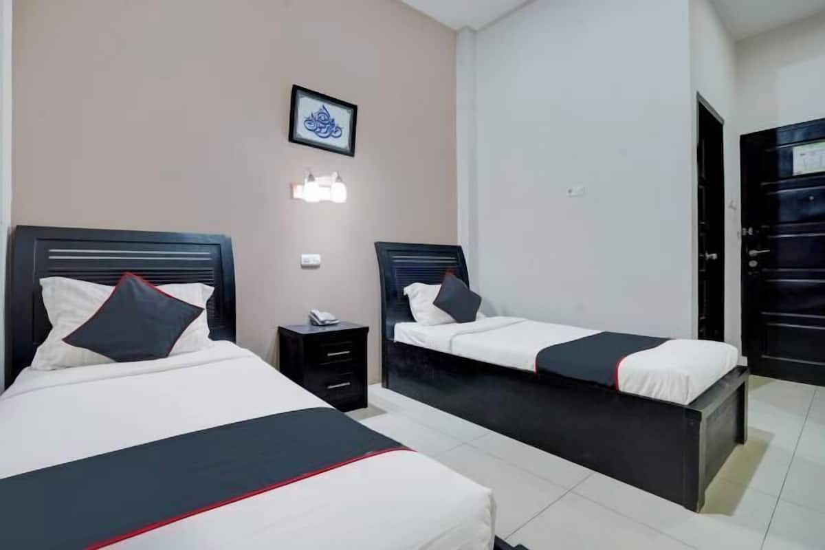 Une chambre d’hôtel avec deux lits, une table de chevet, une lampe fixée au mur et une porte.