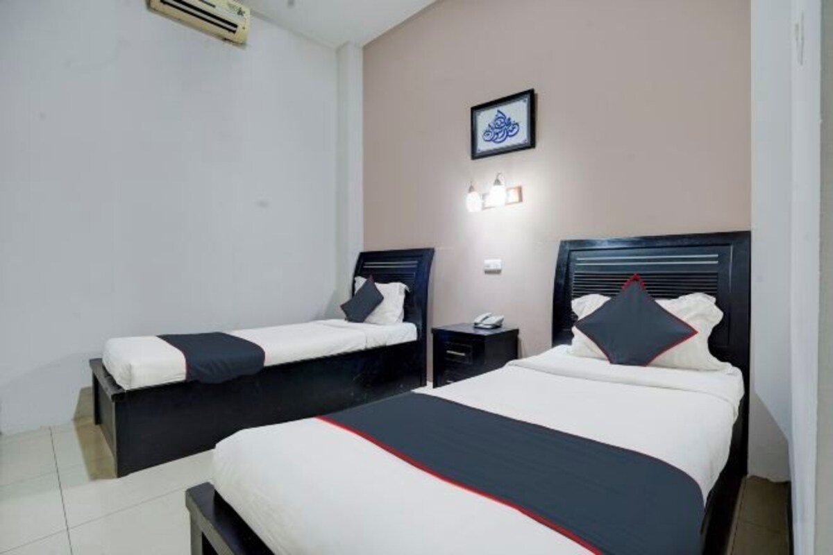 A hotel room with two beds, a small bedside table with a phone, a wall-mounted light, and a framed picture.