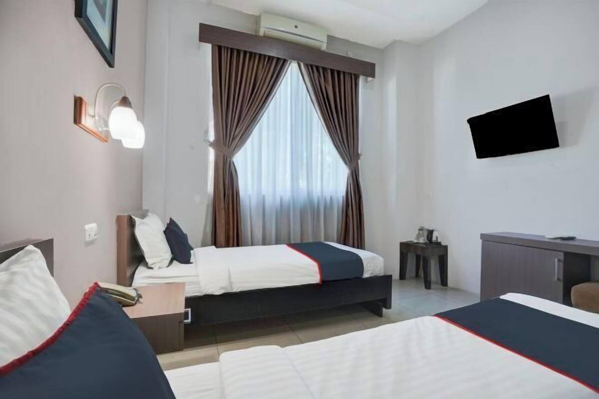 Une chambre d’hôtel avec deux lits, un bureau, une chaise, une télévision et une fenêtre avec des rideaux.