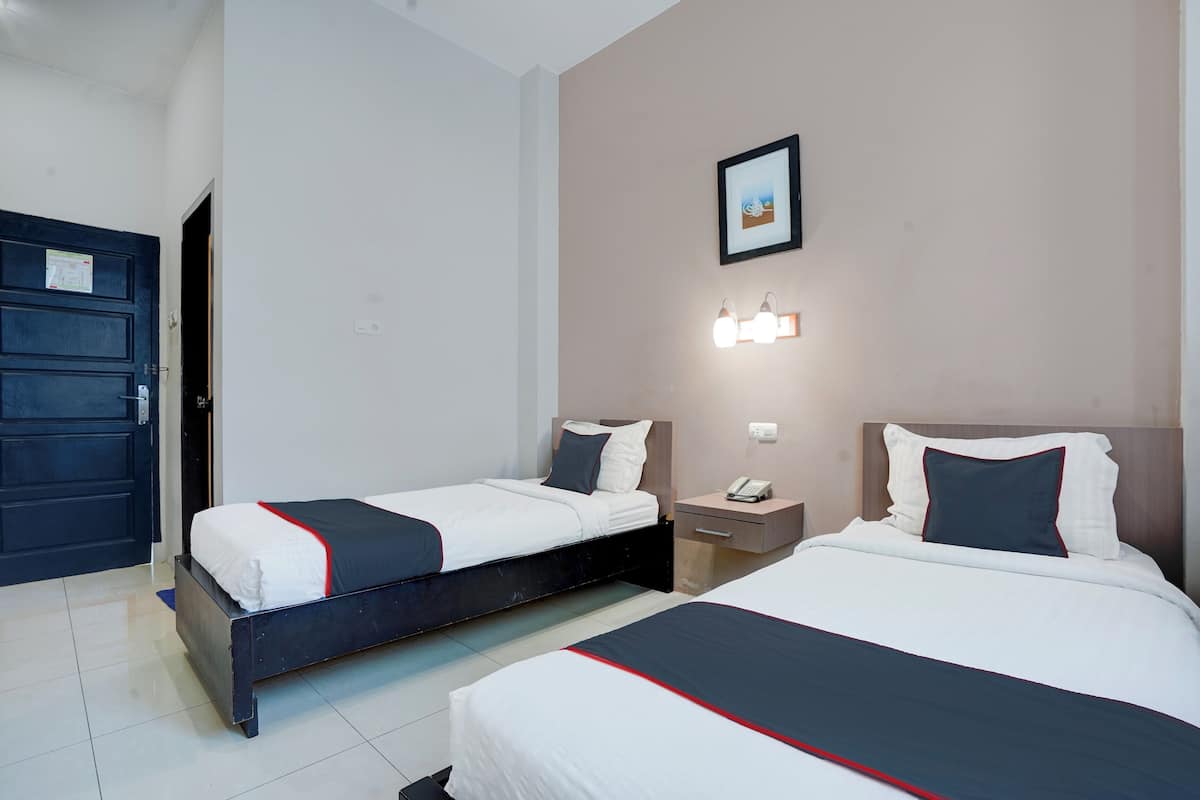 Une chambre d’hôtel avec deux lits, une table de chevet, une commode, un tableau encadré au mur et une porte.