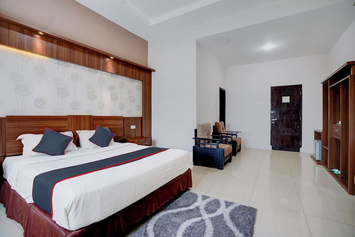 Une chambre d’hôtel avec un grand lit, une tête de lit en bois, un bureau avec une chaise, une armoire et une porte donnant sur une autre pièce.