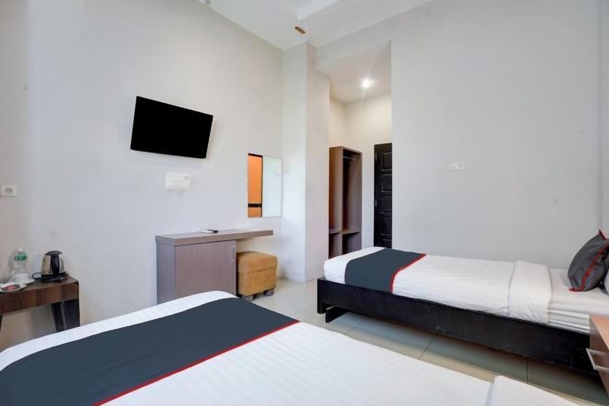 A hotel room with two beds, a desk, a chair, a TV mounted on the wall, and a wardrobe.