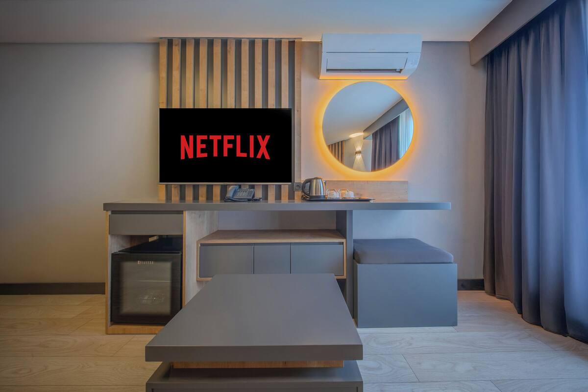 A modern hotel room with a flat-screen TV displaying 'NETFLIX', a built-in coffee maker, a small table, and a seating area.