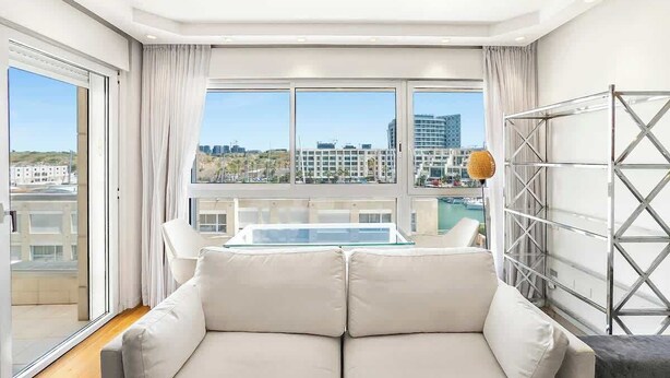 A modern living room with a sofa, a glass table, and a view of the cityscape.