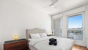 A bedroom with a bed, bedside table, lamp, and a view through large windows.