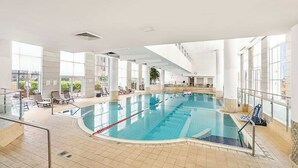 An indoor swimming pool with clear water, surrounded by tiled flooring and glass railings.