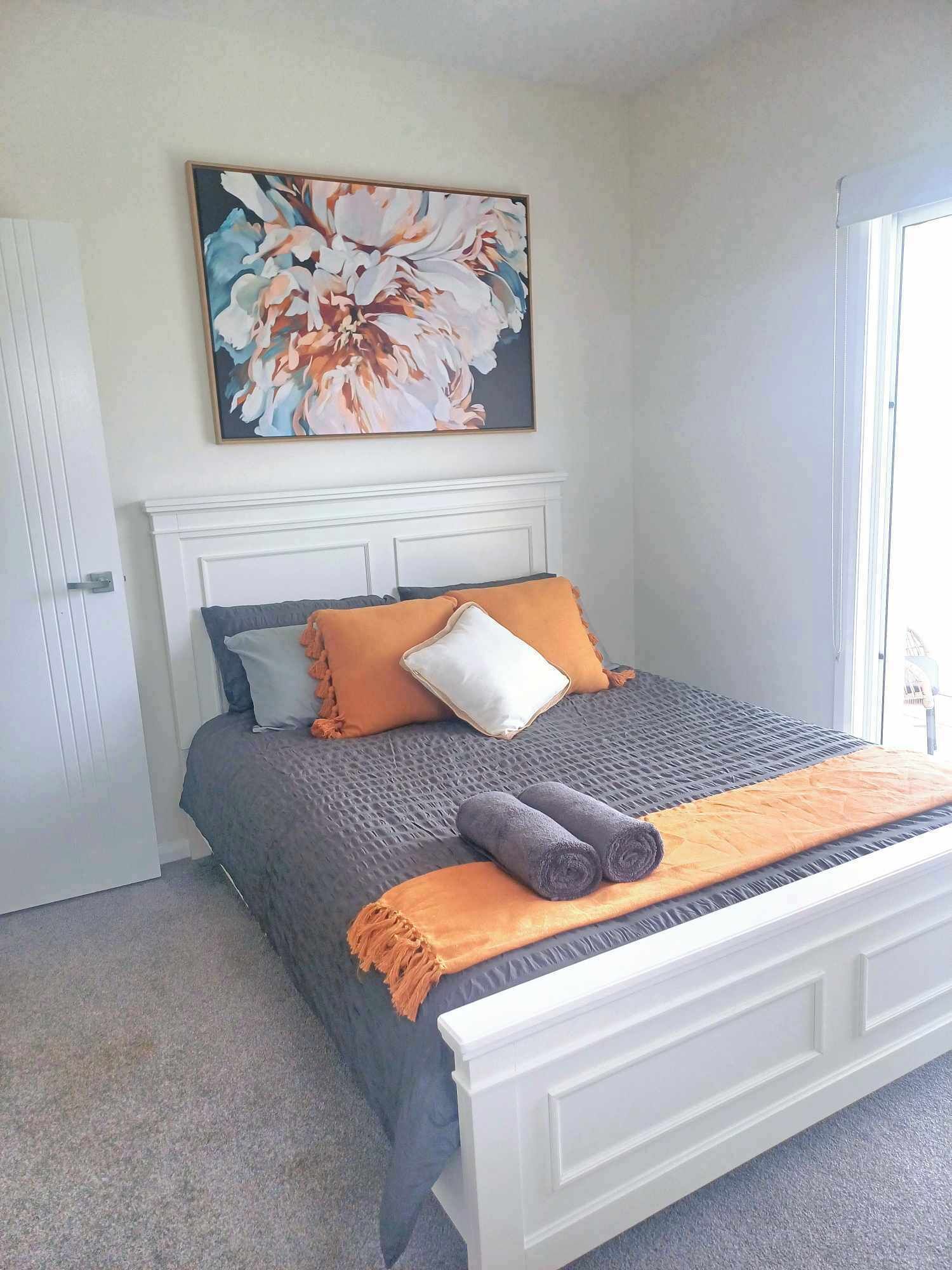 A bedroom with a bed, a large floral painting, and a white headboard.