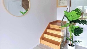 Un interior modern amb una escala de fusta, un mirall rodó i una planta gran en test.