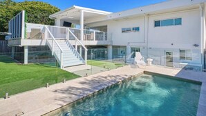 Una casa moderna de dos pisos amb piscina, un porxo cobert i una escala que condueix a un balcó.
