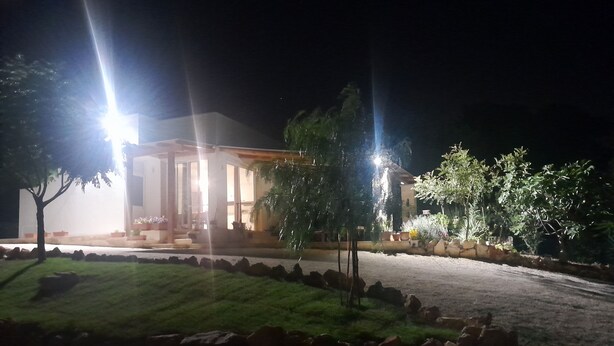 A building with a covered outdoor area, a paved driveway, and a landscaped garden with rocks and trees. - Villa Maresca- countryside house in Carovigno (Puglia)
