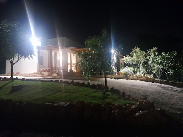 A building with a covered outdoor area, a paved driveway, and a landscaped garden with rocks and trees.
