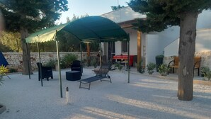 A covered outdoor seating area with a table and chairs, surrounded by trees and a building. - Villa Maresca- countryside house in Carovigno (Puglia)