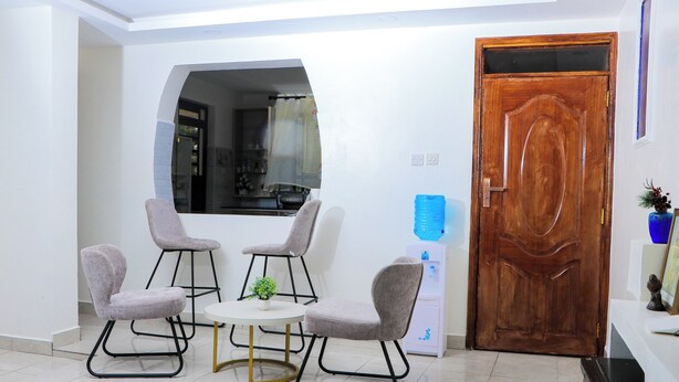 A dining area with a round table and four chairs, a wooden door, and a window with a curtain. - Haven Suites Airbnb Meru (Meru)