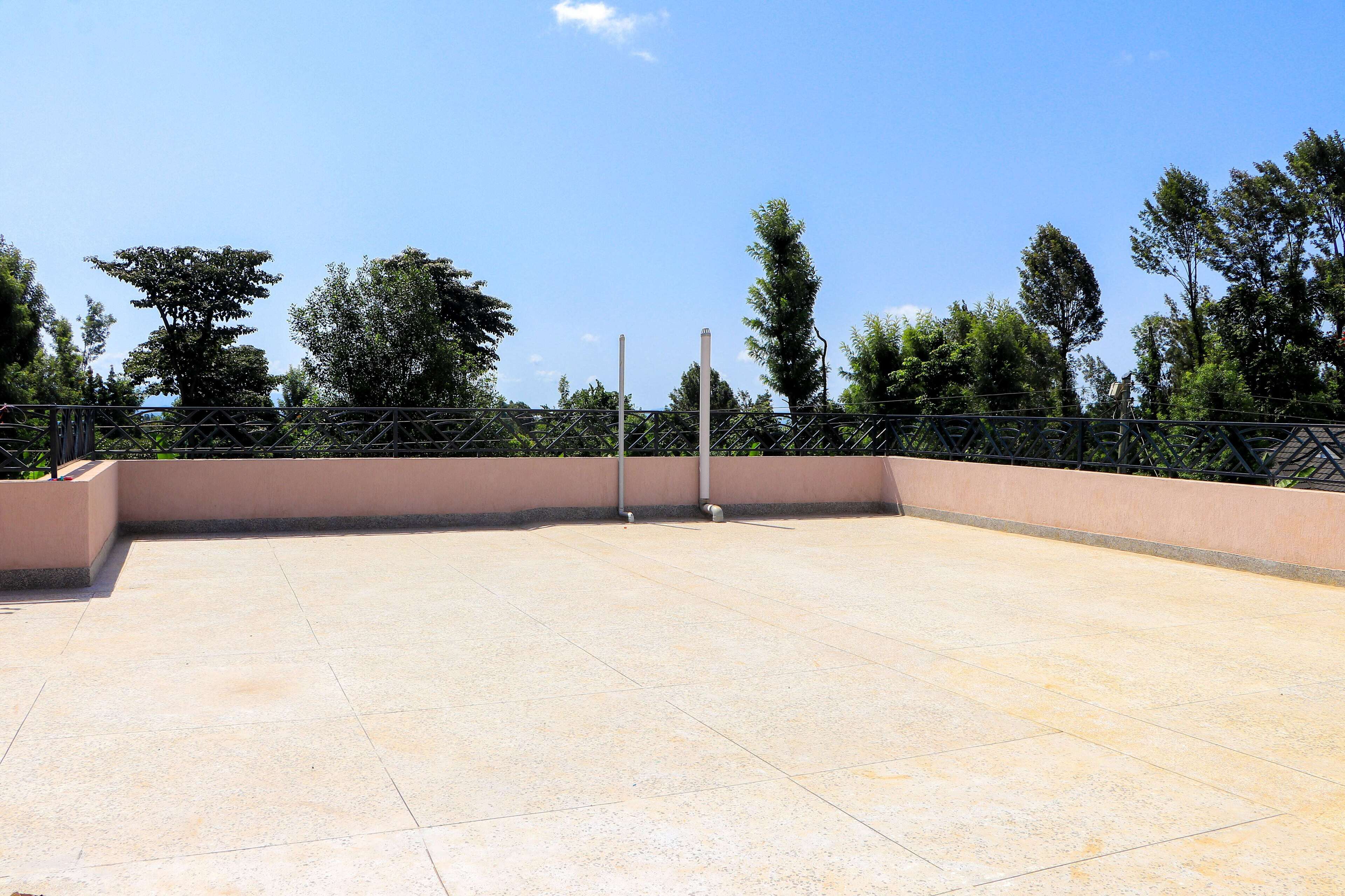 An outdoor terrace with a tiled floor, surrounded by a metal fence and trees.