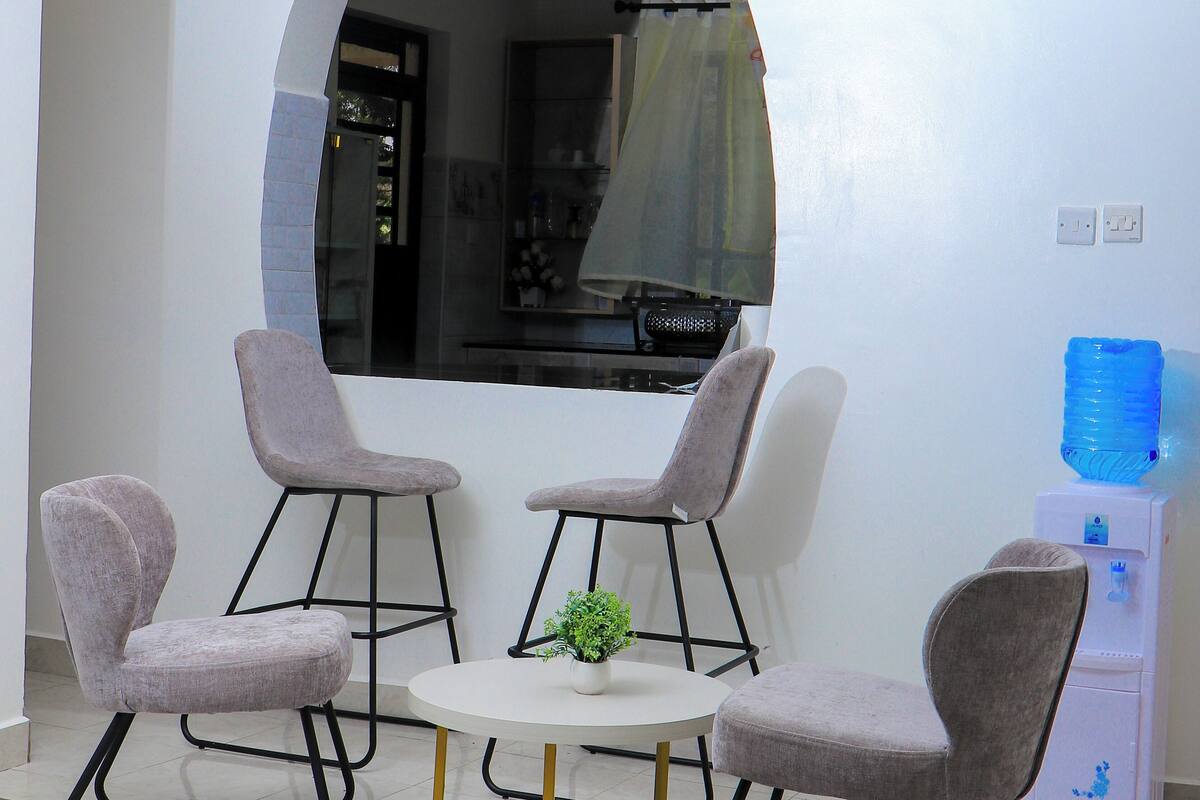 A dining area with a round table and four chairs, a small plant on the table, and a water dispenser in the background.