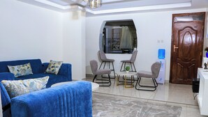 A living room with a blue sofa, two armchairs, a coffee table, and a large mirror. - Haven Suites Airbnb Meru (Meru)