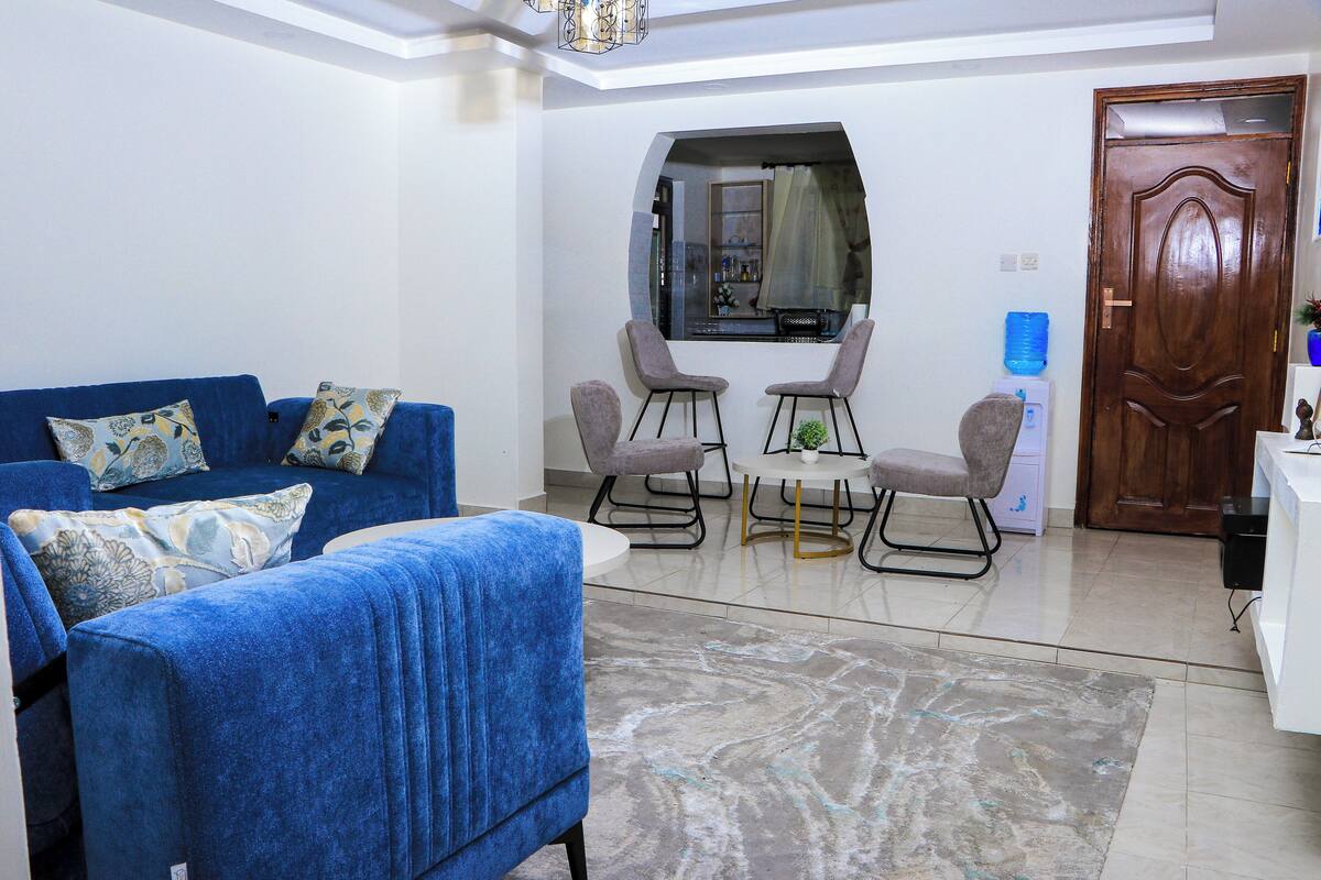 A living room with a blue sofa, two armchairs, a coffee table, and a large mirror.