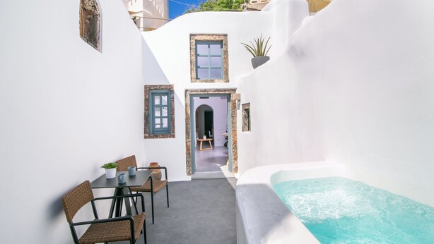 Une petite cour intérieure bordée d’un bâtiment aux murs blancs, un espace repas avec des chaises et une table, et un jacuzzi.