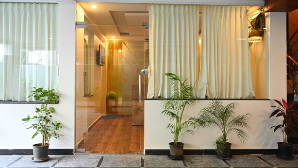 A modern hotel lobby with a glass door entrance, potted plants, and a staircase leading to an upper level. - SHARAN'S INN SUTES & BANQUETS (Hyderabad)