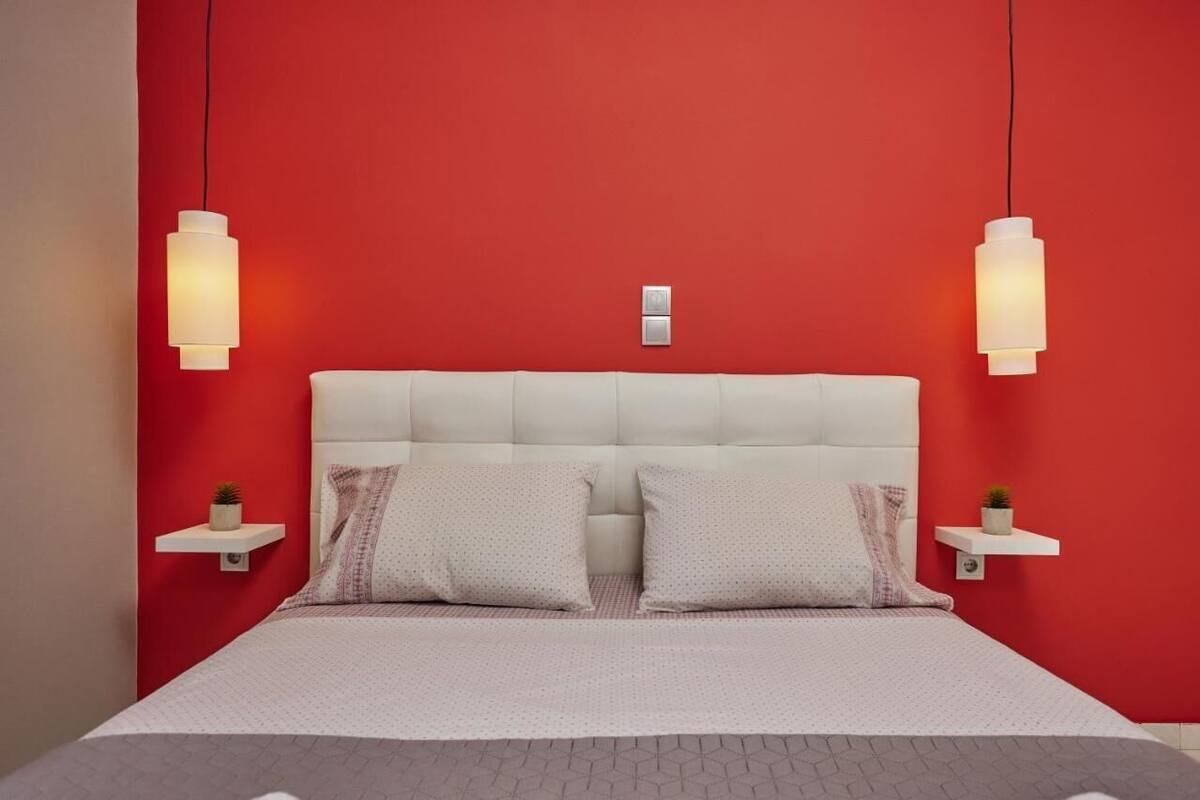 A bedroom with a red wall, white headboard, two bedside tables with lamps, and a bed with pillows.