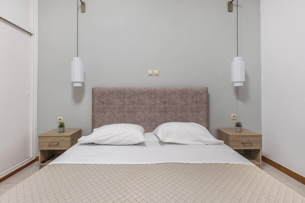 A bedroom with a bed, two bedside tables, a headboard, and two wall-mounted light fixtures.