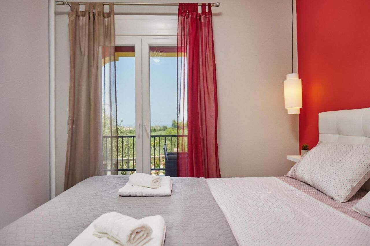 Une chambre d’hôtel avec un lit, une table de chevet, une lampe et une vue sur l’extérieur par une fenêtre munie de rideaux.
