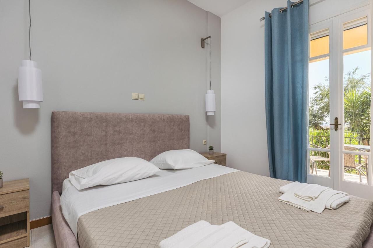 Ein Schlafzimmer mit einem großen Bett, einem Nachttisch, einer Wandlampe und Blick auf Grün durch eine Tür.