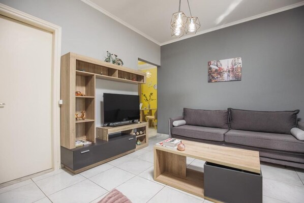 A modern living room with a grey sofa, wooden entertainment unit, and a flat-screen TV. - P.Koklas Apartments (Zakynthos)