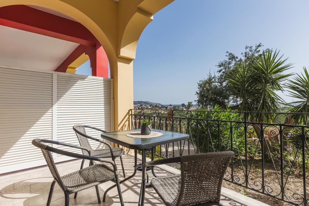 A balcony with wicker chairs and a table, overlooking a garden and distant landscape.