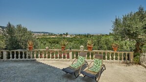 A balcony with two lounge chairs, potted plants, and a view of a green landscape.