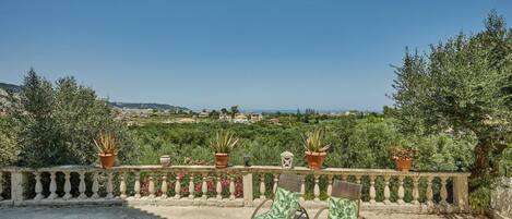 A balcony with two lounge chairs, potted plants, and a view of a green landscape.