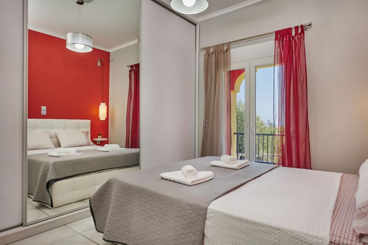 Camera d'albergo con un letto, un letto più piccolo, un balcone con tende rosse e una finestra vista.