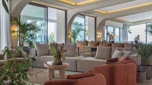 Una sala de estar moderna con un sofá, sillones y una mesa de centro. Hay ventanas amplias y plantas en macetas.