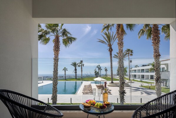 Un balcón con vista a una piscina, palmeras y un paisaje urbano distante.