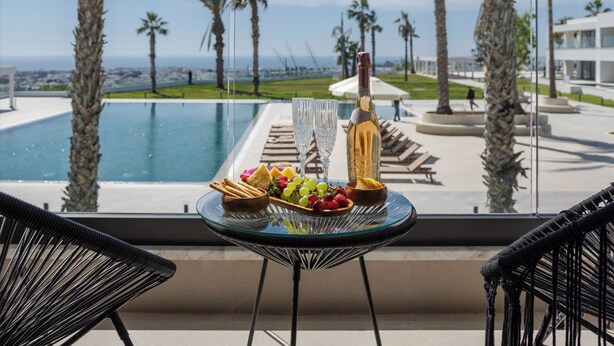 Un balcón con una mesa dispuesta para comer, con vista a una piscina y palmeras.