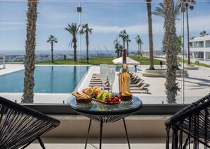 Un balcon avec une table dressée pour un repas, donnant sur une piscine et des palmiers.