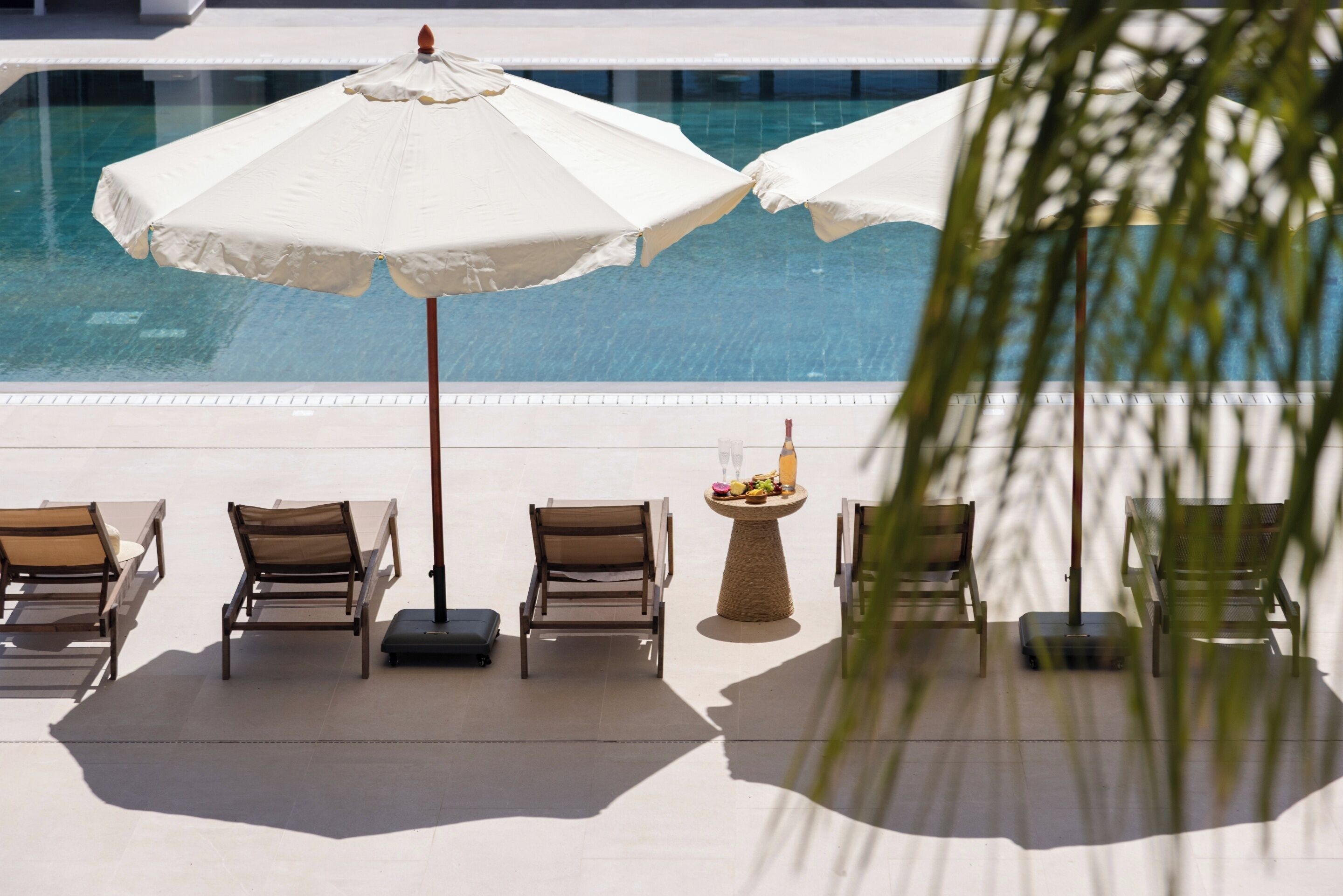 Zona de piscina con sillones reclinables, sombrillas y una mesa con una bebida.