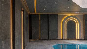 A modern indoor pool area with dark marble walls, illuminated by vertical light strips and a circular light feature.