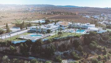 Un resort con varias construcciones, una piscina y montañas al fondo.