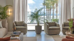 Una sala de estar moderna con dos sillones, un sofá, una planta grande en maceta y vistas a palmeras y al mar.