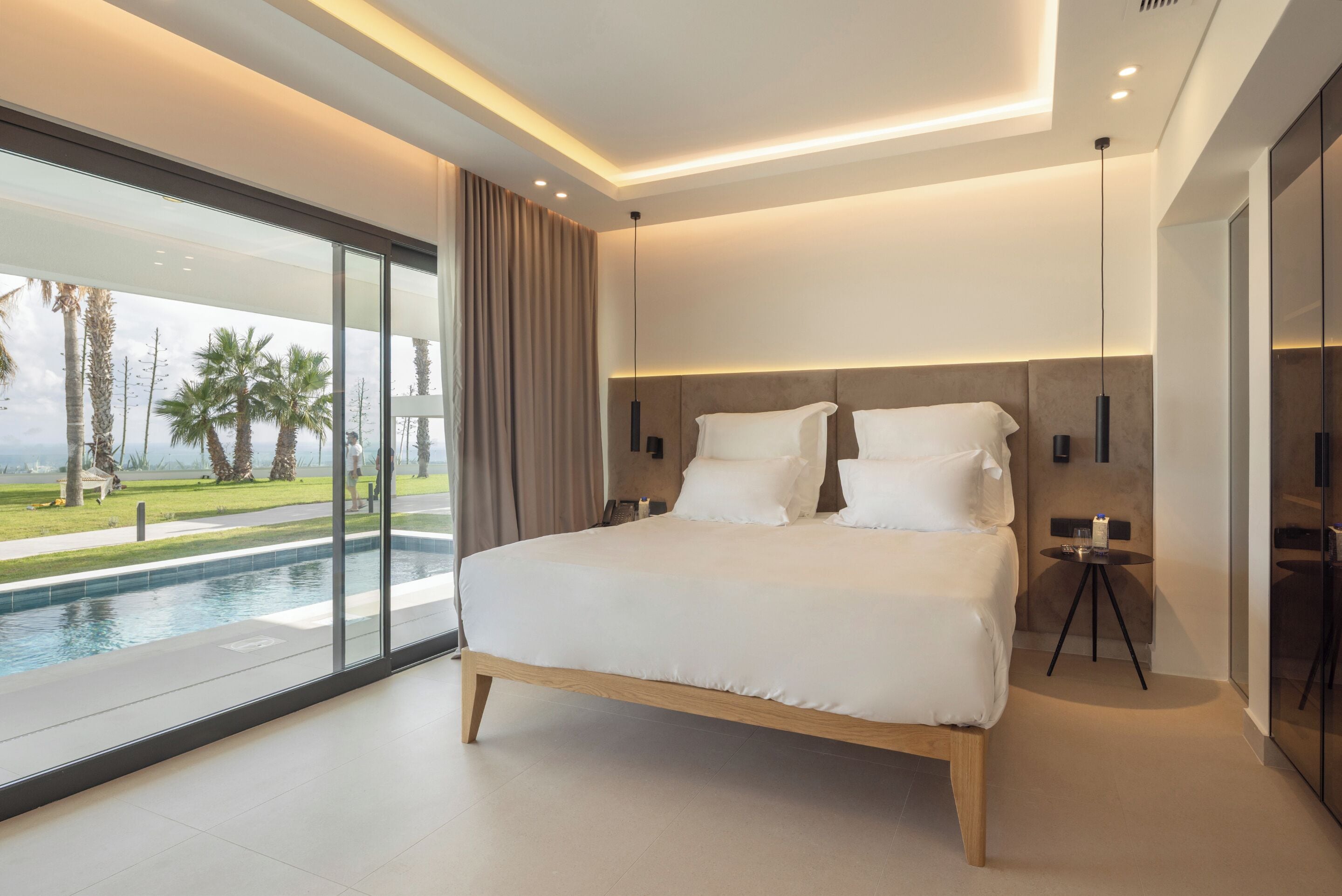 A modern bedroom with a large bed, a view of a swimming pool, and a balcony.