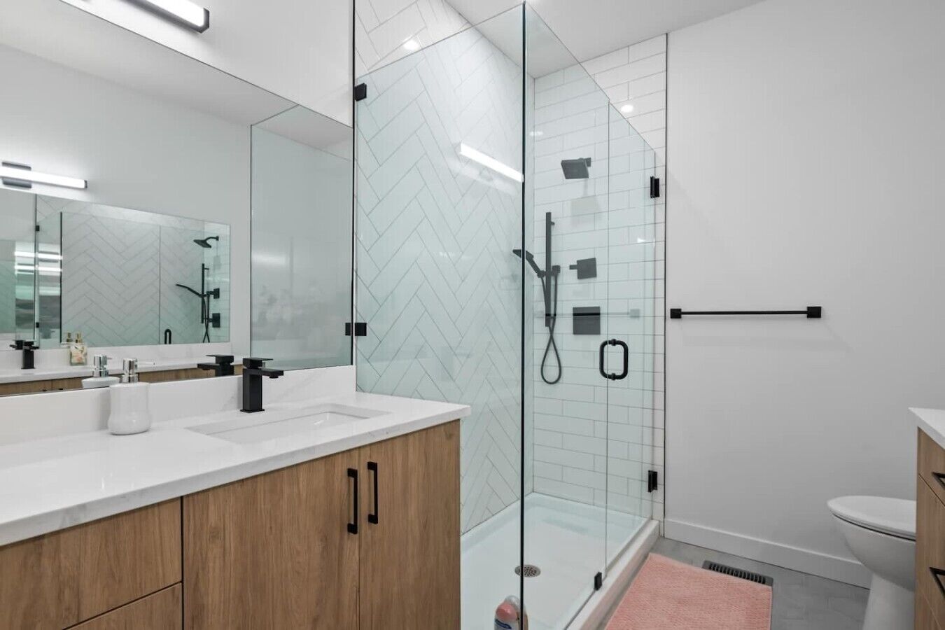 A modern bathroom with a glass-enclosed shower, a large mirror, and wooden cabinets.