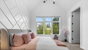 A bedroom with a bed, a window, a potted plant, and a door.